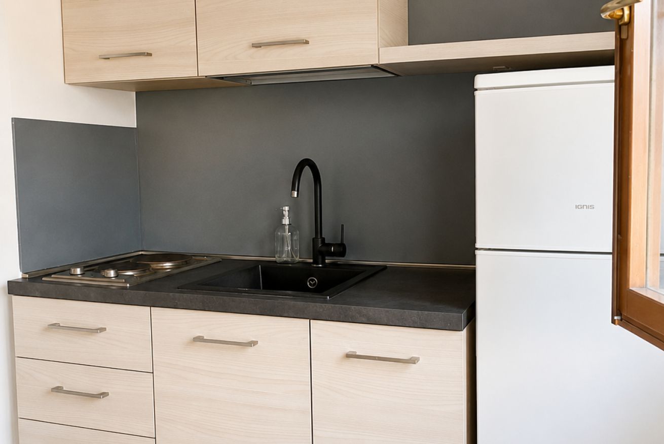 A kitchen with a black sink, a white refrigerator, and light wooden cabinets.