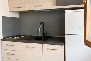 Eine Küche mit einem schwarzen Spülbecken, einem weißen Kühlschrank und hellen Holzschränken.