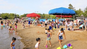 Ein überfüllter Strand mit Menschen und spielenden Kindern, Sonnenschirmen und Liegestühlen.