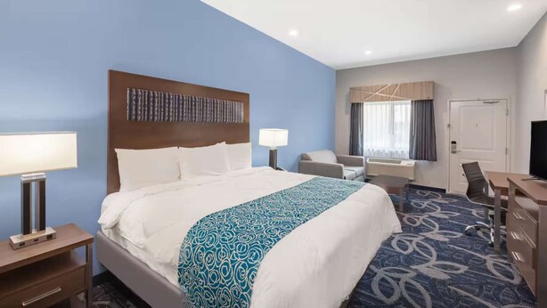 A hotel room with a large bed, a desk, a chair, a TV, and a window with curtains. - Stay Near Airport with Free Breakfast & Parking (Houston)