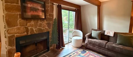 Una sala de estar con chimenea de piedra, un sofá, un sillón y una alfombra colorida.