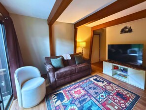 Ein Wohnzimmer mit einer Couch, einem Sessel, einem Fernseher und einem gemusterten Teppich.