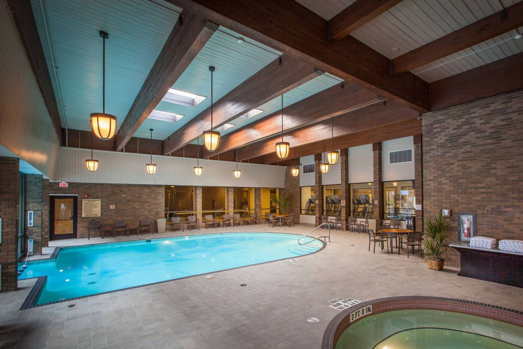 An indoor swimming pool with a tiled floor, surrounded by seating areas and a brick wall.