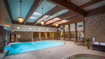 An indoor swimming pool with a tiled floor, surrounded by seating areas and a brick wall.