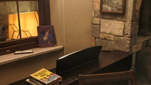 A room with a stone wall, a fireplace, a window with a lamp, and a table with a book and a chair. - Stunning Private Panorama Suite within a 350m² Luxury Villa – Full Bay View" (Muğla)