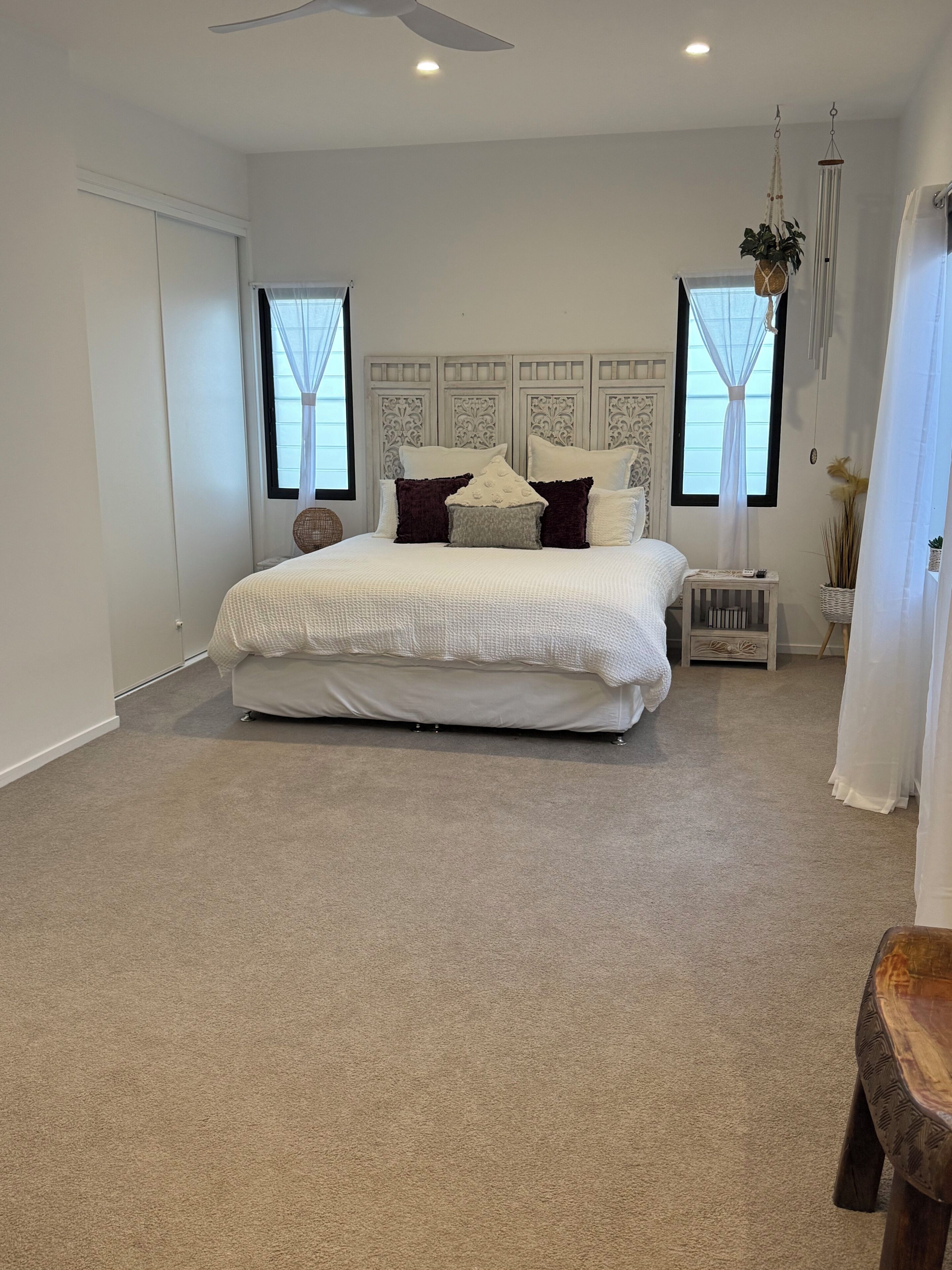 Une chambre avec un grand lit, un ventilateur de plafond et deux fenêtres ornées de rideaux légers.