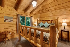 Ein Zimmer in einer Holzhütte mit Bett, Fenster, Lampe und einem Bild an der Wand.
