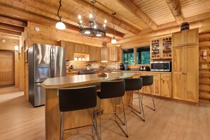 A modern kitchen with wooden cabinets, stainless steel appliances, and a bar area with stools. - Misty Mountain River House*Fire Pit*Private Cabin (Tillamook)