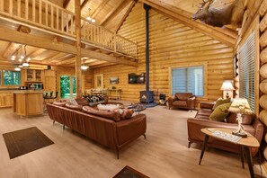 A log cabin interior with a fireplace, leather sofas, wooden flooring, and a kitchen area. - Misty Mountain River House*Fire Pit*Private Cabin (Tillamook)