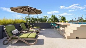 Et tagområde med pool, liggestole, et bord og en parasol.