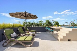 Ein Poolbereich auf dem Dach mit Liegestühlen, einem Tisch und einem Sonnenschirm.