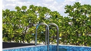 A swimming pool with metal ladders, surrounded by lush green foliage. - Ocean Boutique Condos (Playa del Carmen)