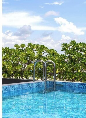 Ein Schwimmbecken mit Metallleitern, umgeben von üppiger, grüner Vegetation.