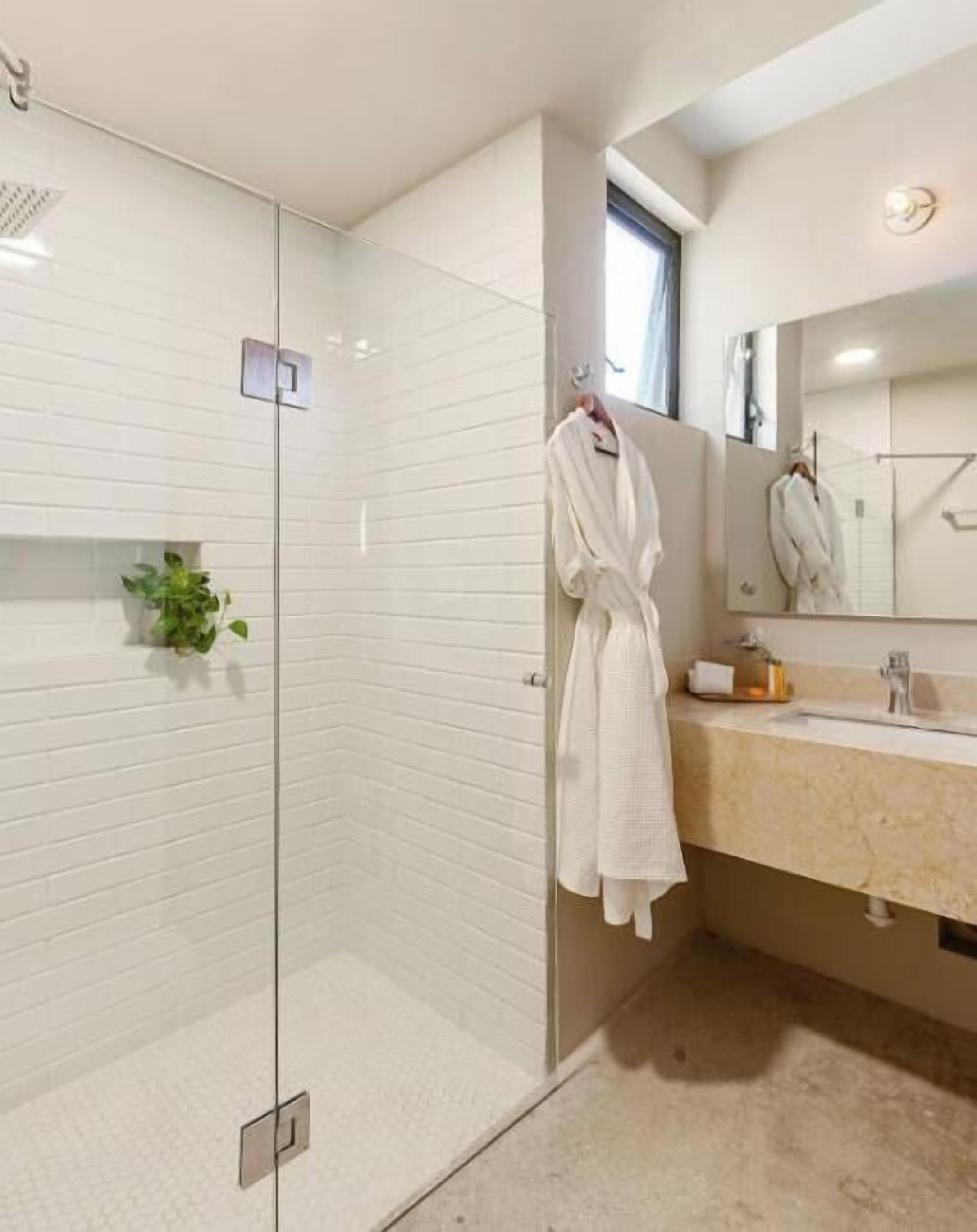 Un baño moderno con cabina de ducha de vidrio, tocador color beige y un espejo grande.