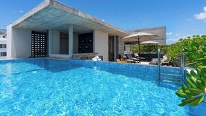 En pool med solstolar och parasoller, ett avskärmat sittområde och en byggnad med en modern arkitektonisk stil.