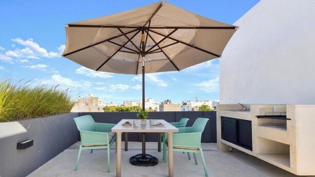 Terrassa exterior amb taula i caires, una gran ombrel·la i una barbacoa de disseny.