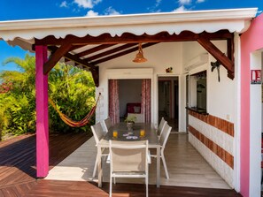 A covered outdoor dining area with a table and chairs, a hammock, and a view of the surrounding greenery. - Villa Hibalya (Saint-François)