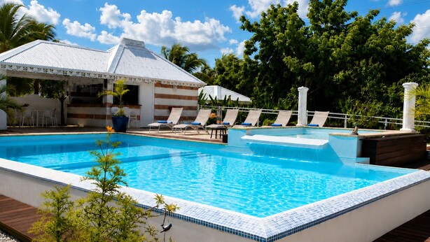 Ein rechteckiger Swimmingpool mit einer gefliesten Kante, umgeben von Liegestühlen und einer überdachten Sitzgelegenheit mit einem gestreiften Sonnensegel.