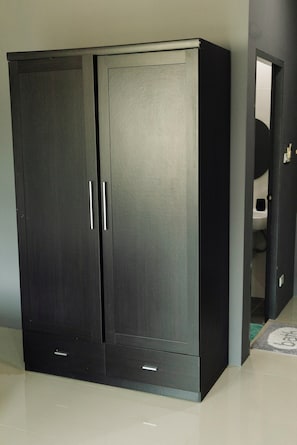 A large, dark-colored wardrobe with two doors and two drawers, located in a hallway with a tiled floor. - The One Rawai Rooms (Rawai)