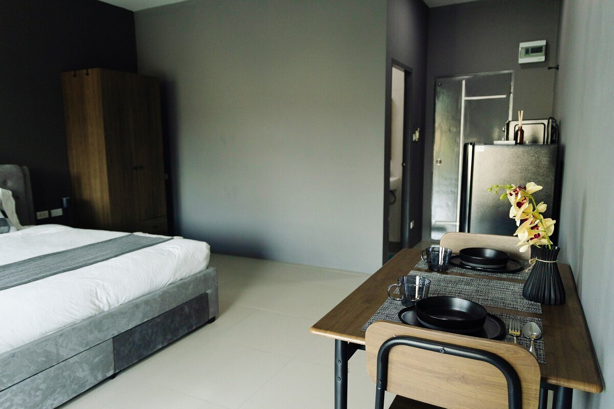 A modern hotel room with a bed, a desk with a chair, a mirror, and a vase with flowers.