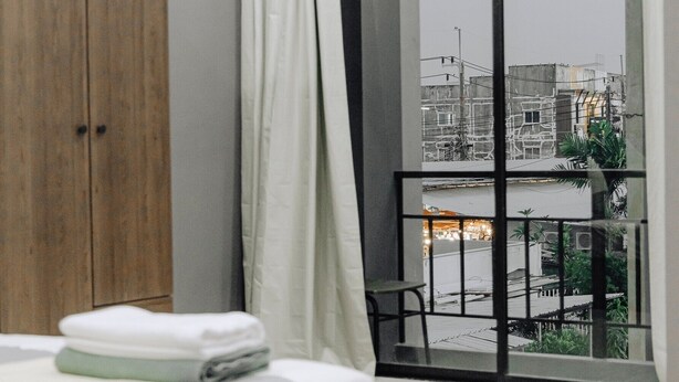 Ein modernes Schlafzimmer mit einem Bett, einem Holzschrank, einem Fenster mit Blick auf Gebäude und einer Klimaanlage.