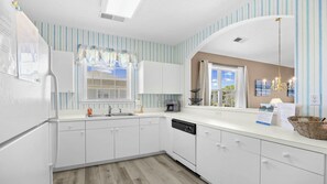 A modern kitchen with white cabinets, a dishwasher, a coffee maker, and a window with striped curtains. - 931 Wedgewood - Barefoot Resort Rentals (North Myrtle Beach)