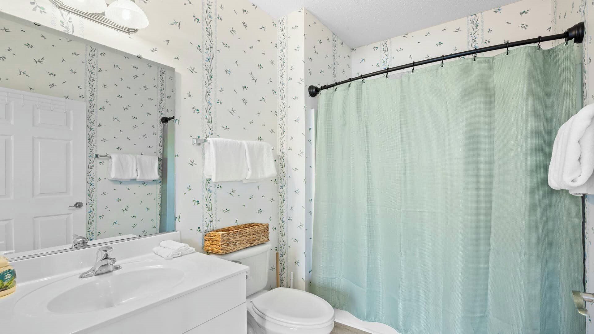 Ein Badezimmer mit weißem Waschbecken, Toilette, Spiegel und Duschvorhang.