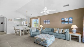 A modern living room with a sofa, ottoman, and dining area. - 931 Wedgewood - Barefoot Resort Rentals (North Myrtle Beach)