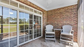 A patio with two Adirondack chairs, a small table, and a brick wall. - 613 Wedgewood - Barefoot Resort Rentals (North Myrtle Beach)