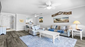 Ein geräumiges Wohnzimmer mit Deckenventilator, einer Sofagarnitur, einem Couchtisch und einem Essbereich mit Tisch und Stühlen.