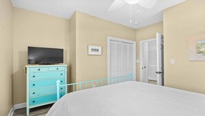 Ein Schlafzimmer mit Bett, Kommode, Fernseher, Tür und Deckenventilator.