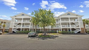 Ein mehrstöckiges Hotel mit Balkonen, einem zentralen Baum und einem Parkplatz.