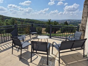 A balcony with outdoor furniture, a view of a green landscape, and a clear sky.