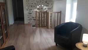 Una habitación con pared de piedra, una puerta de madera, un sillón negro y una lámpara.