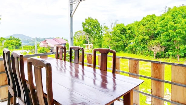 A covered outdoor dining area with a table and chairs, surrounded by a wooden fence, overlooking a lush green landscape. - Guntur Homestay Labuan Bajo (Manggarai Barat)