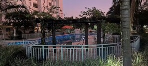 A pool area with a pergola, surrounded by a fence and palm trees. - Fully equipped apartment (Riocentro / Olympic Park) (Rio de Janeiro)