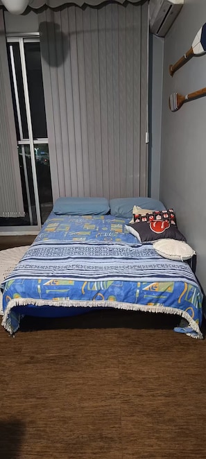 A bedroom with a bed, a window with blinds, a wall-mounted air conditioner, and a door. - Fully equipped apartment (Riocentro / Olympic Park) (Rio de Janeiro)