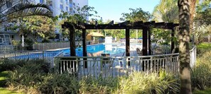 A pool area with a pergola, lounge chairs, and a view of a building in the background. - Fully equipped apartment (Riocentro / Olympic Park) (Rio de Janeiro)