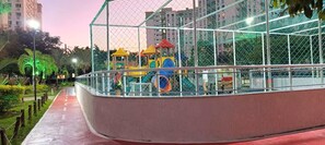 Un parque infantil rodeado por una valla de metal con un sendero rojo que lleva a él.