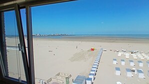 A beach view from inside a building with a clear sky, a sandy beach, and a row of beach huts. - Beachfront Knokke-Heist Studio w/ Oceanfront Views (Knokke-Heist)