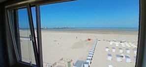A beach view from inside a building with a clear sky, a sandy beach, and a row of beach huts. - Beachfront Knokke-Heist Studio w/ Oceanfront Views (Knokke-Heist)