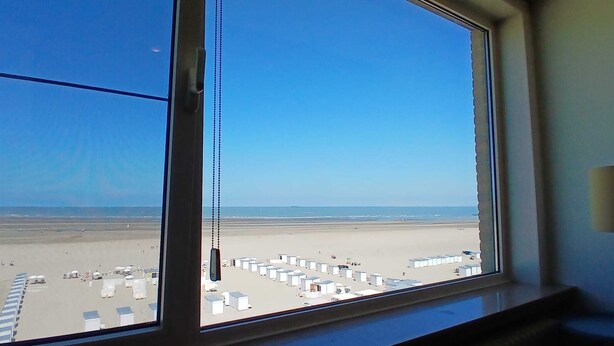 A view of a beach with a clear sky, a sandy shore, and a row of white buildings in the distance. - Beachfront Knokke-Heist Studio w/ Oceanfront Views (Knokke-Heist)