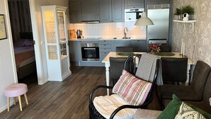 A compact living space with a kitchenette, a dining area with a table and chairs, and a small seating area with a chair and stool. - 4 Star Holiday Home in Uddevalla (Uddevalla)