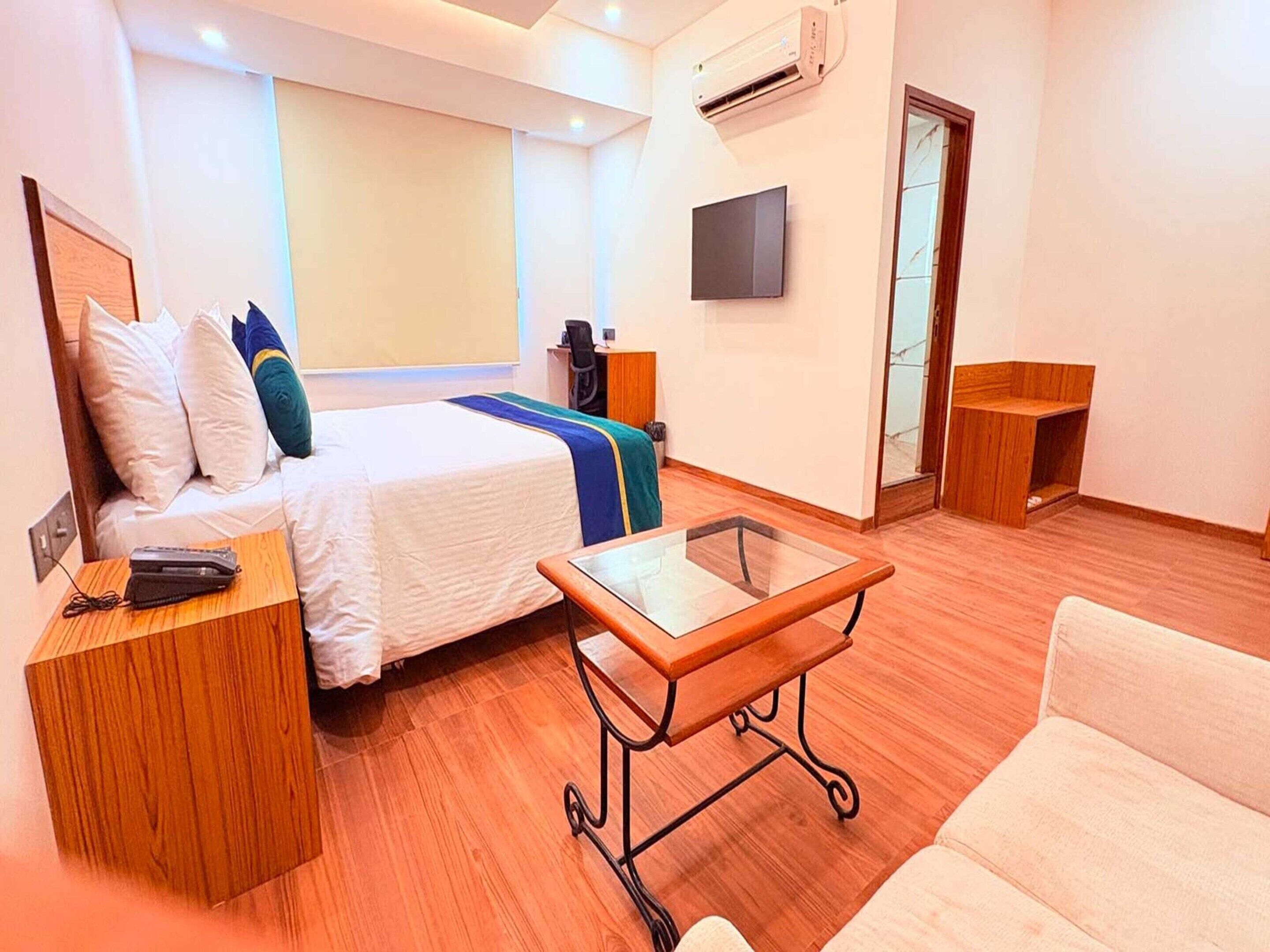Ein Hotelzimmer mit Bett, Schreibtisch, Stuhl, Fernseher und Klimaanlage.