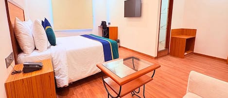 A hotel room with a bed, a desk, a chair, a TV, and an air conditioning unit.