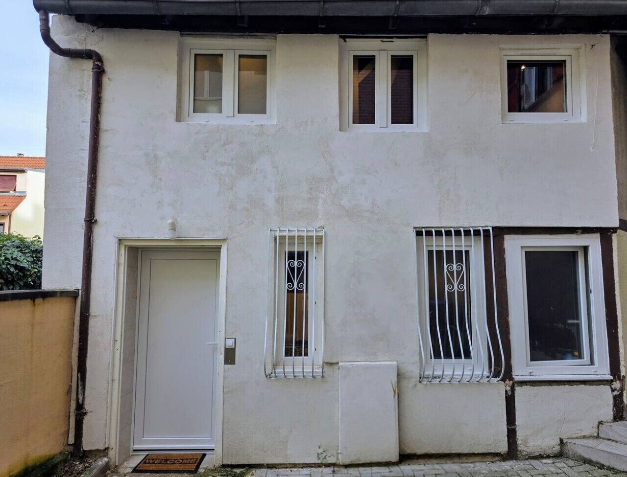 Ein Gebäude mit weißer Fassade, einer Tür und zwei Fenstern mit Metallgitter.