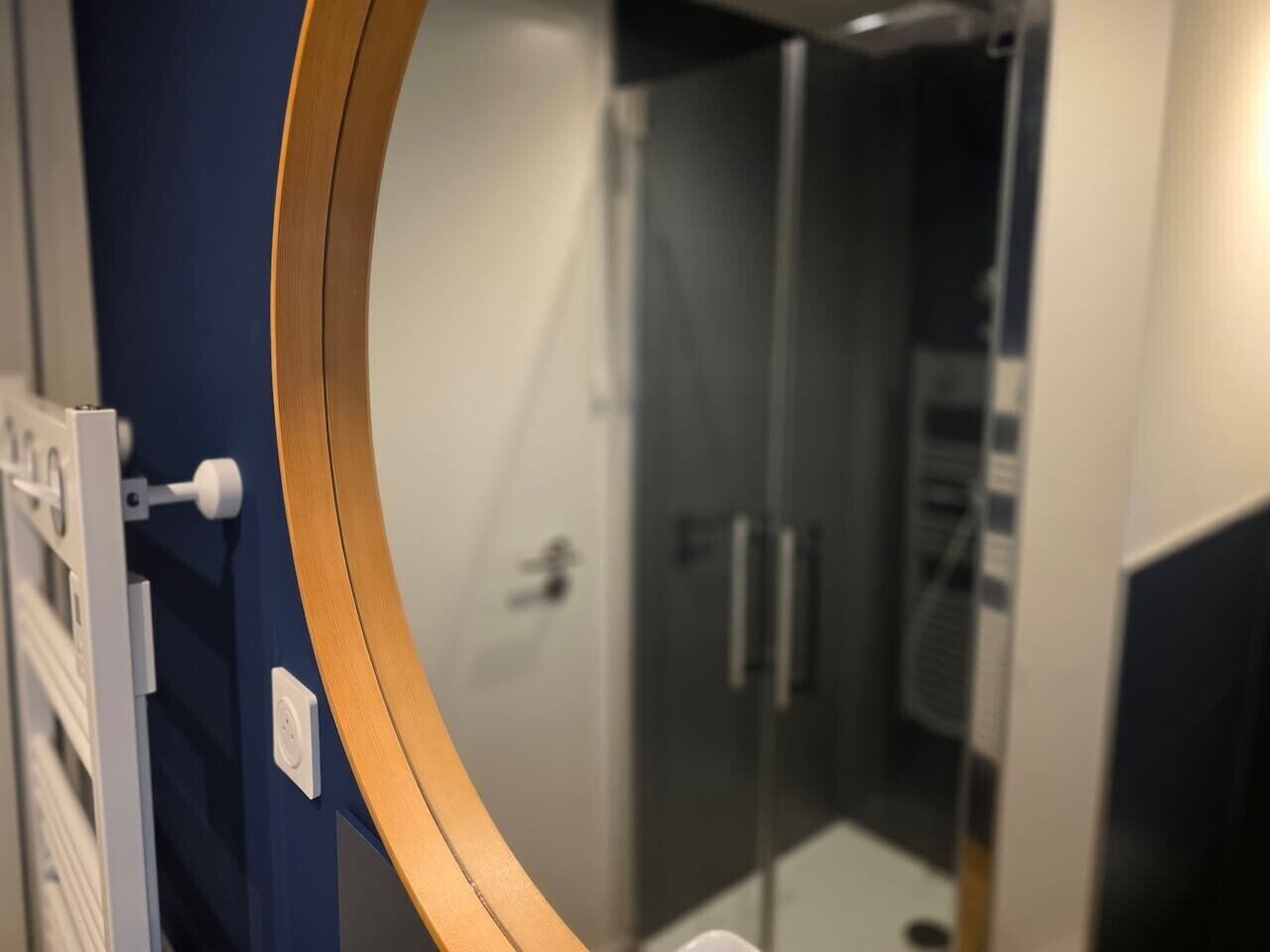 Ein Badezimmer mit Duschkabine aus Glas, einem spiegel mit Holzrahmen und blauen Wänden.