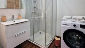 Een moderne badkamer met een glazen douchecabine, een wastafel met een houten kastje en een voorlader wasmachine.