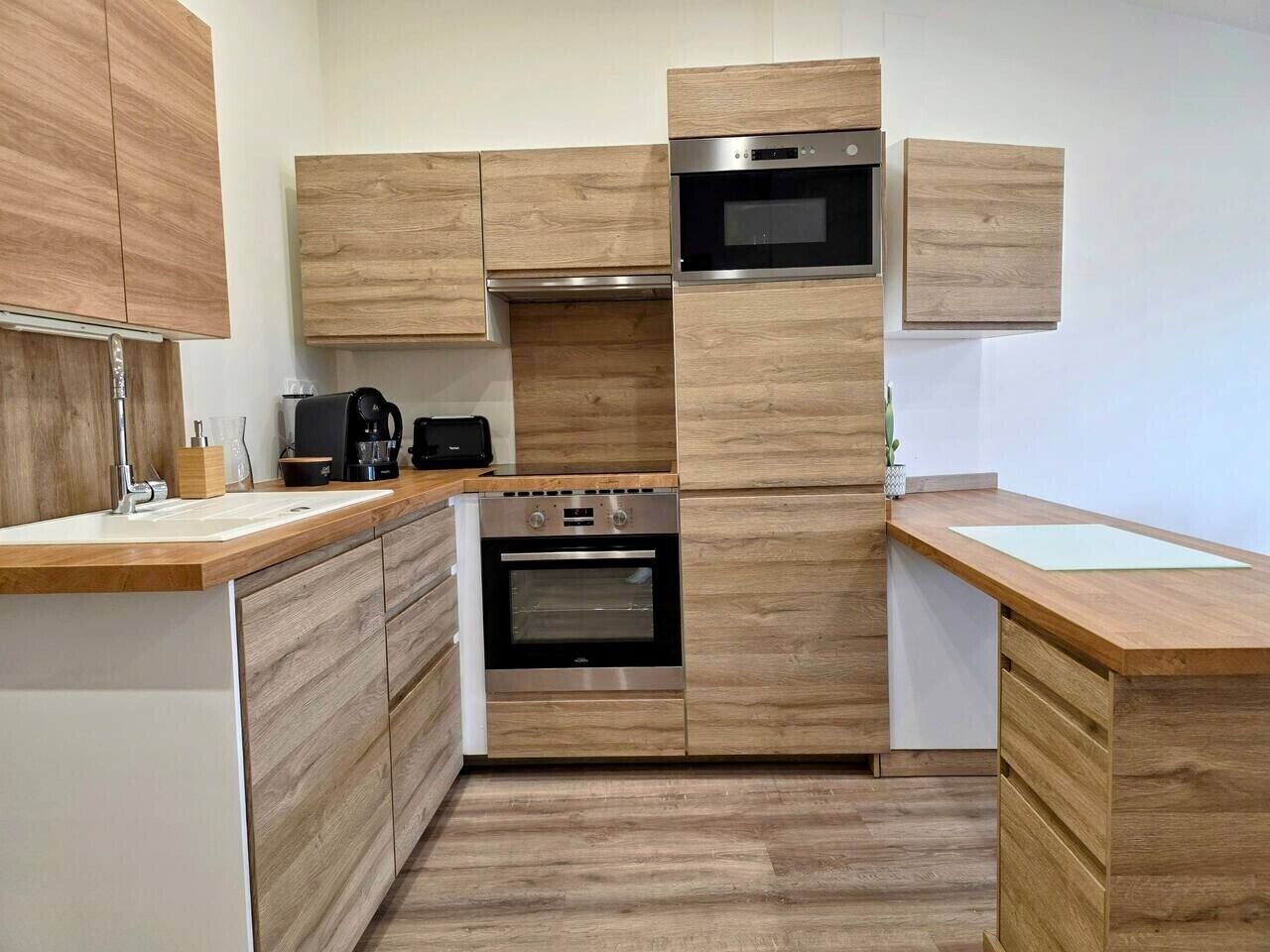 Eine moderne Küche mit Holzschränken, einem eingebauten Backofen und einer Mikrowelle.