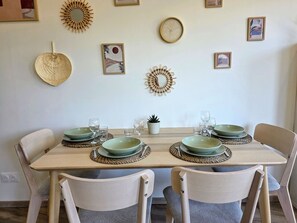 Una tavola imbandita per quattro, con piatti verdi e bicchieri trasparenti, circondata da sedie dai toni chiari.